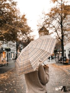 Personne avec un parapluie se promenant dans une rue pluvieuse bordée de feuilles d'automne et d'arbres.