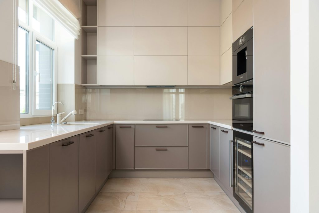Intérieur d'une cuisine moderne lumineuse avec placards et four avec micro-ondes près d'un évier avec robinet à côté d'une fenêtre