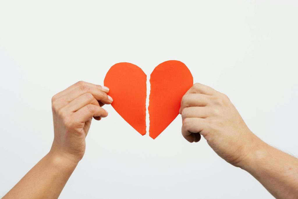 Un gros plan de mains tenant un cœur en papier rouge déchiré, symbolisant une peine de cœur ou des problèmes relationnels.