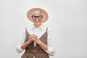 Femme senior élégante souriant avec confiance dans une tenue stylée avec chapeau et lunettes
