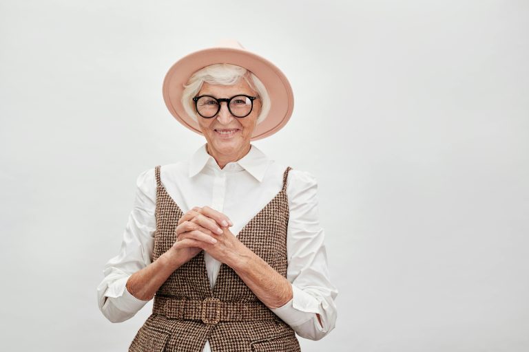Femme senior élégante souriant avec confiance dans une tenue stylée avec chapeau et lunettes