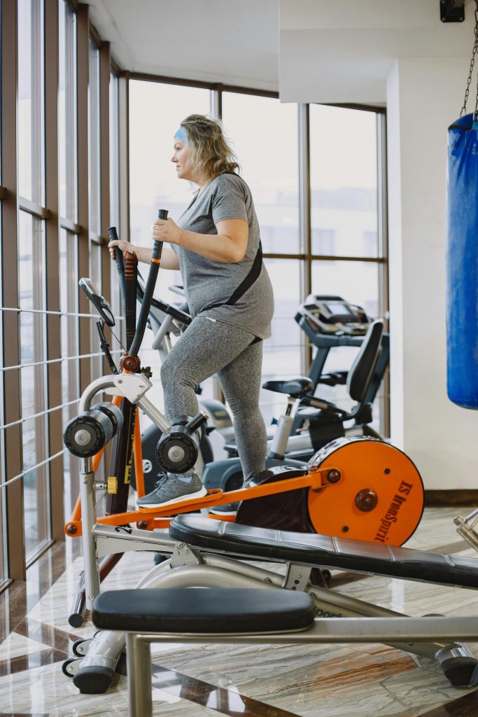 Une femme adulte utilisant un vélo elliptique dans une salle de sport moderne et lumineuse.