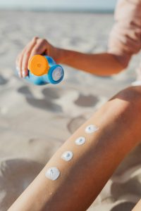 Woman appliquant de la crème solaire sur sa jambe à la plage. Routine de soins estivaux pour une protection solaire en extérieur.