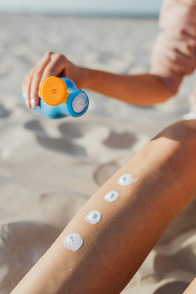 Woman appliquant de la crème solaire sur sa jambe à la plage. Routine de soins estivaux pour une protection solaire en extérieur.