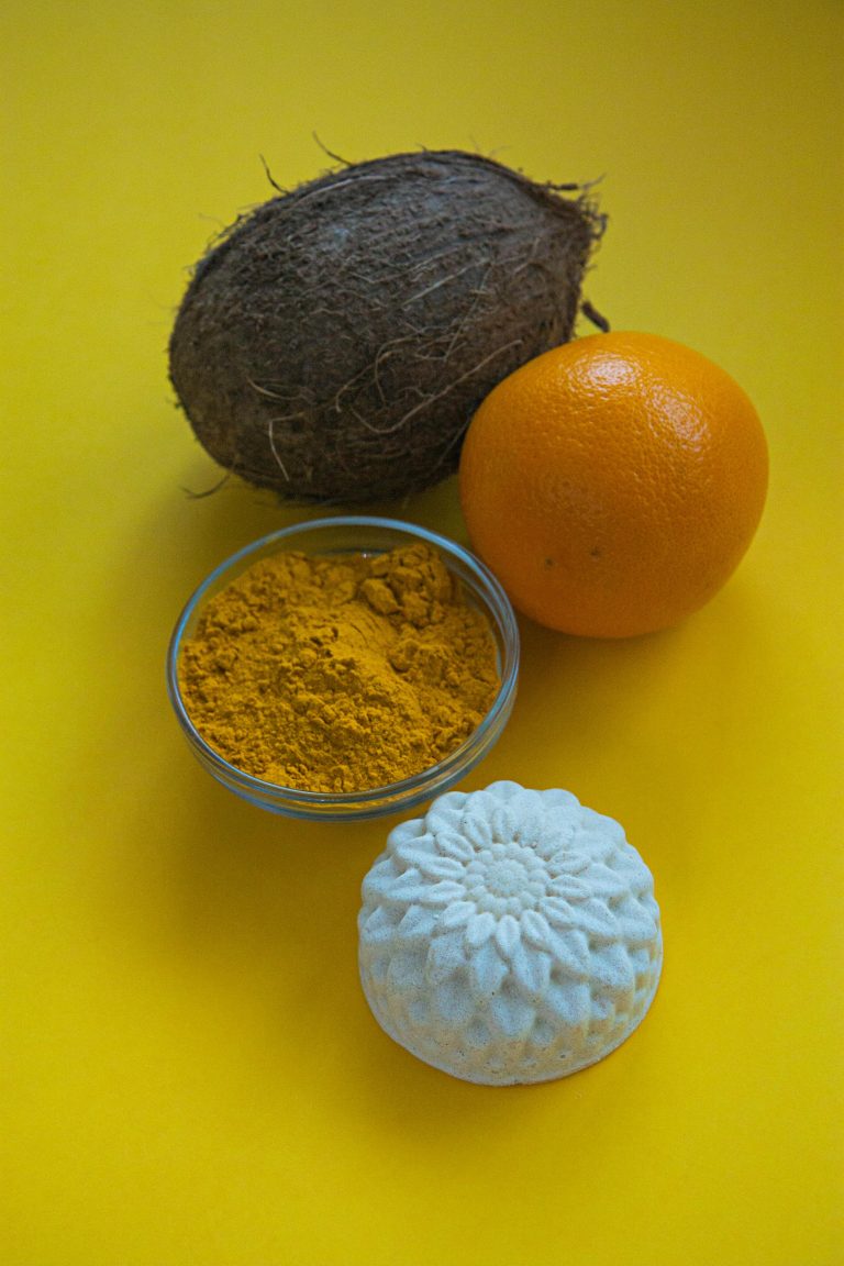 Vibrant arrangement of coconut, orange, and turmeric on yellow background. Arrangement vibrant de noix de coco, d'orange et de curcuma sur fond jaune.