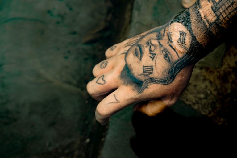 A detailed shot of a hand with expressive tattoos including Roman numerals and faces. Un gros plan détaillé d'une main avec des tatouages expressifs incluant des chiffres romains et des visages.