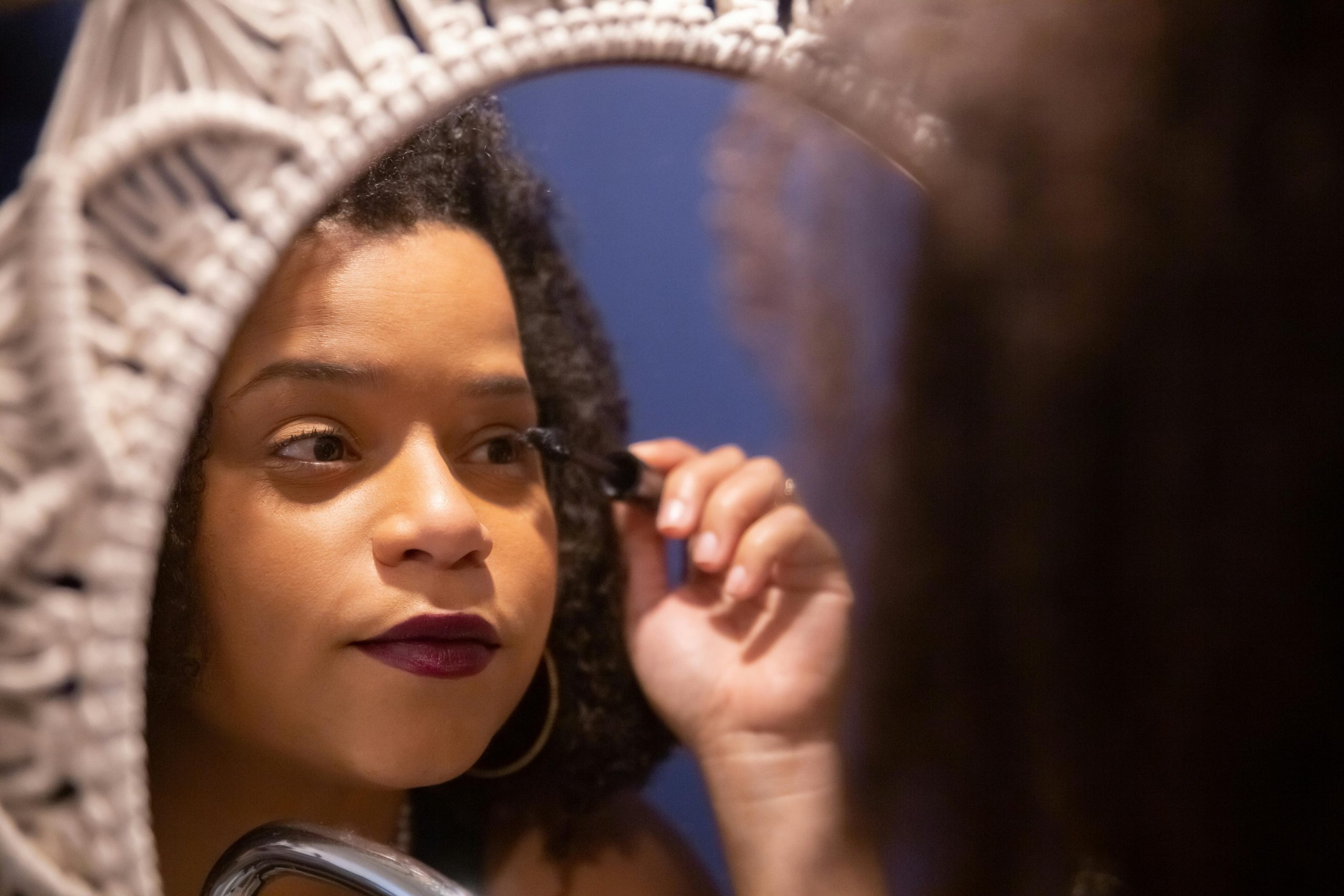 Close-up of a woman applying mascara in a mirror reflection, emphasizing beauty and care. Gros plan d'une femme appliquant du mascara dans le reflet d'un miroir, soulignant la beauté et les soins.