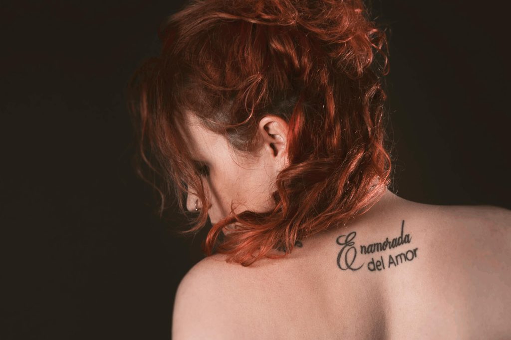 Artistic portrait of a redhead woman with back tattoo in a studio setting. Portrait artistique d'une femme rousse avec un tatouage dans le dos dans un studio.
