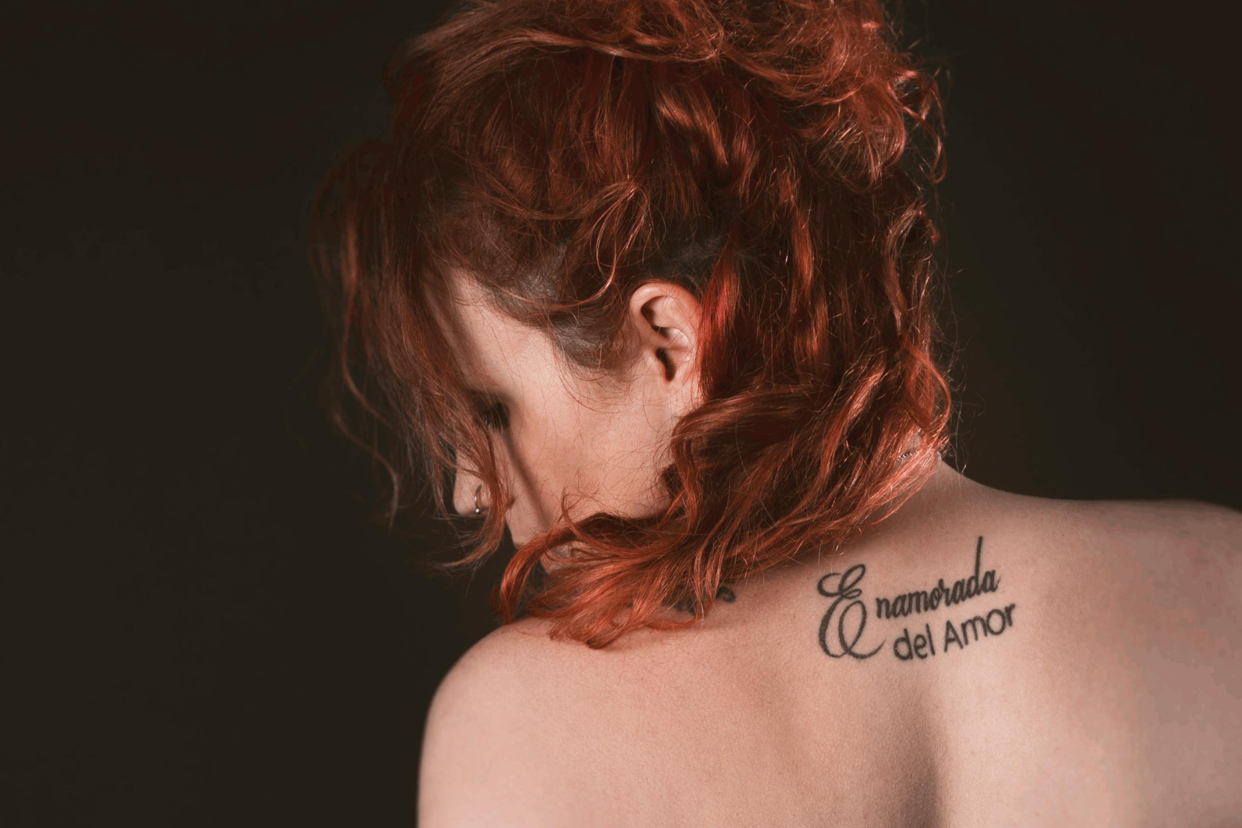Artistic portrait of a redhead woman with back tattoo in a studio setting. Portrait artistique d'une femme rousse avec un tatouage dans le dos dans un studio.