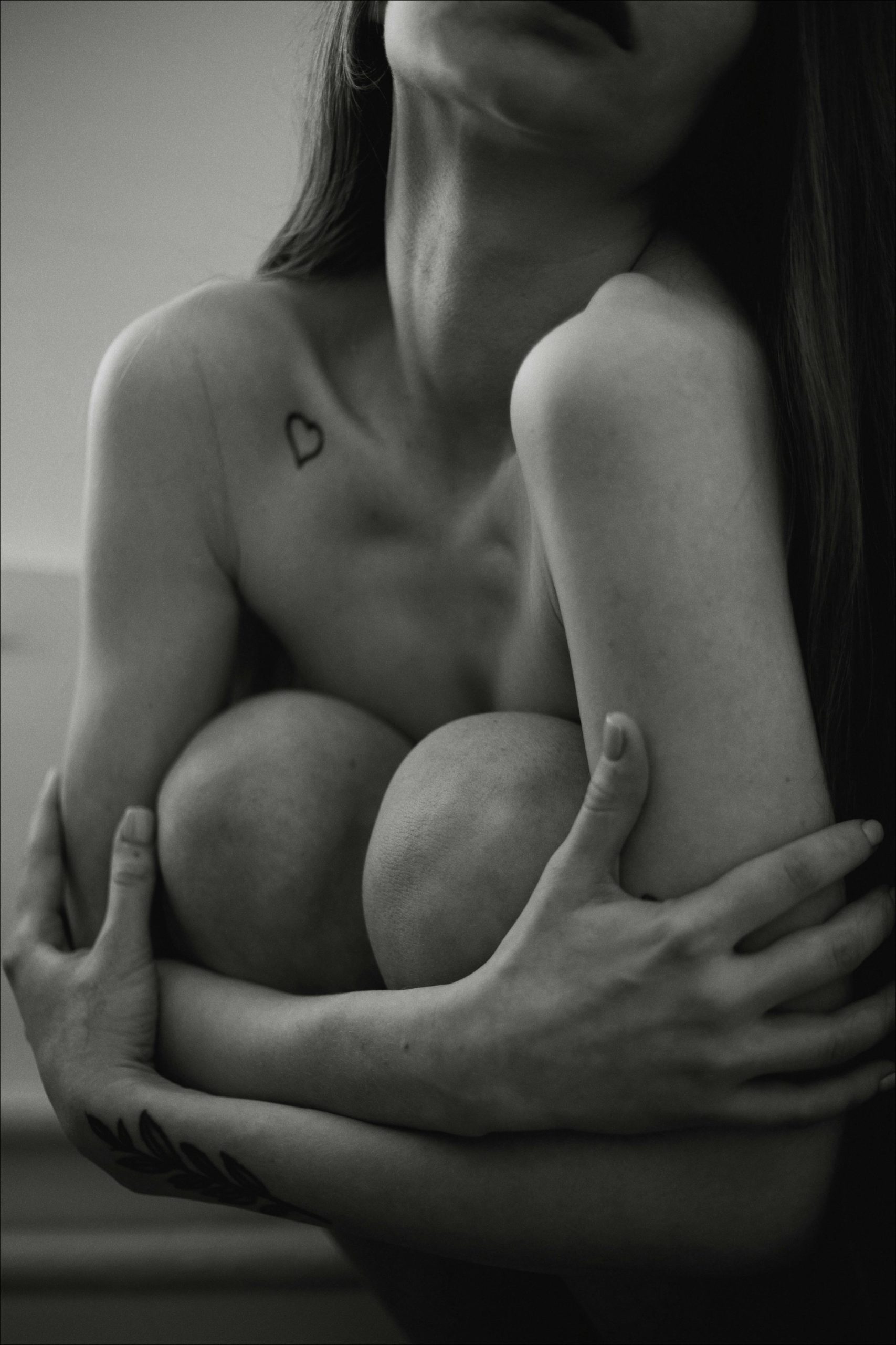 Emotive black and white portrait of a woman embracing her knees, showcasing body art. Portrait en noir et blanc émouvant d'une femme s'enlaçant les genoux, mettant en valeur l'art corporel.
