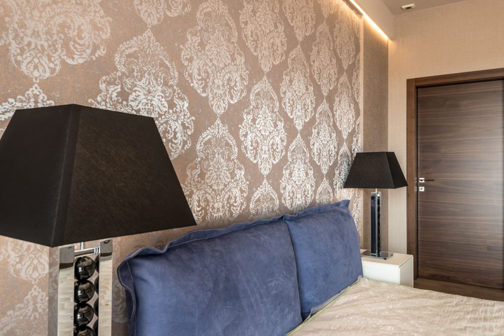 Modern bedroom with elegant wallpaper design, blue pillows, and stylish black lamps. Chambre moderne avec design de papier peint élégant, oreillers bleus et lampes noires élégantes.