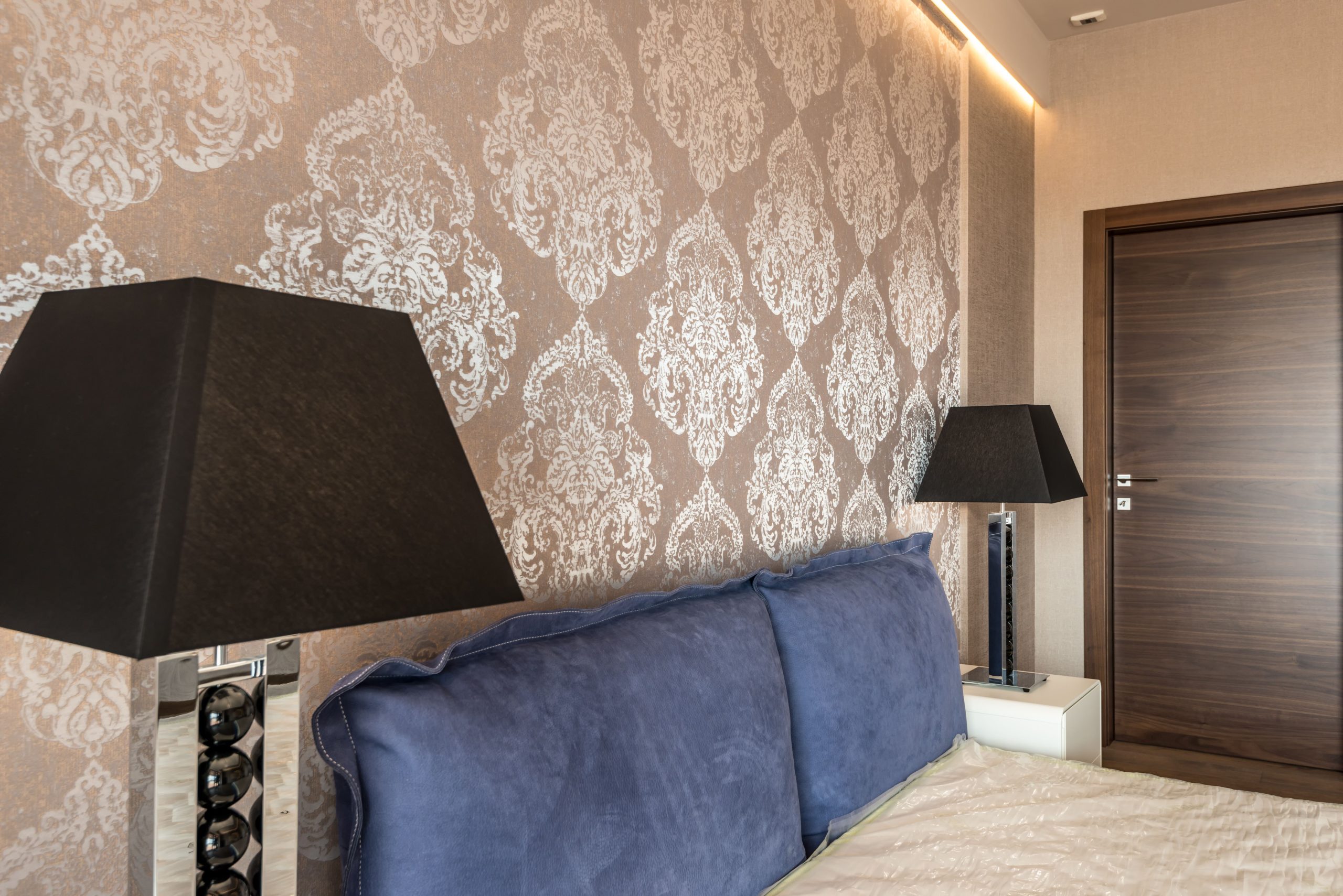 Modern bedroom with elegant wallpaper design, blue pillows, and stylish black lamps. Chambre moderne avec design de papier peint élégant, oreillers bleus et lampes noires élégantes.