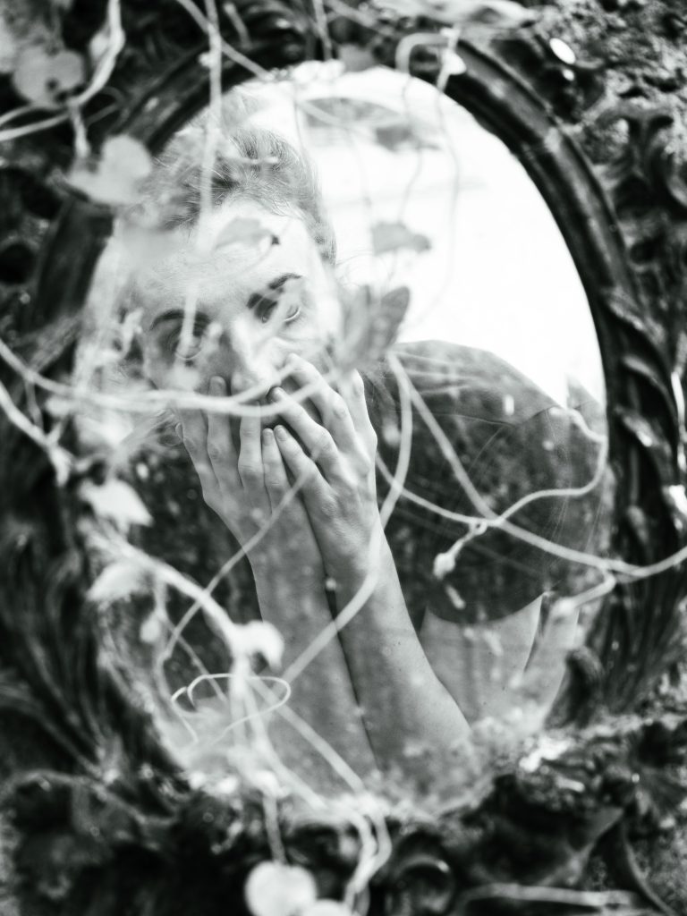 Artistic reflection of a woman in a vintage mirror surrounded by ivy. Reflet artistique d'une femme dans un miroir vintage entouré de lierre.