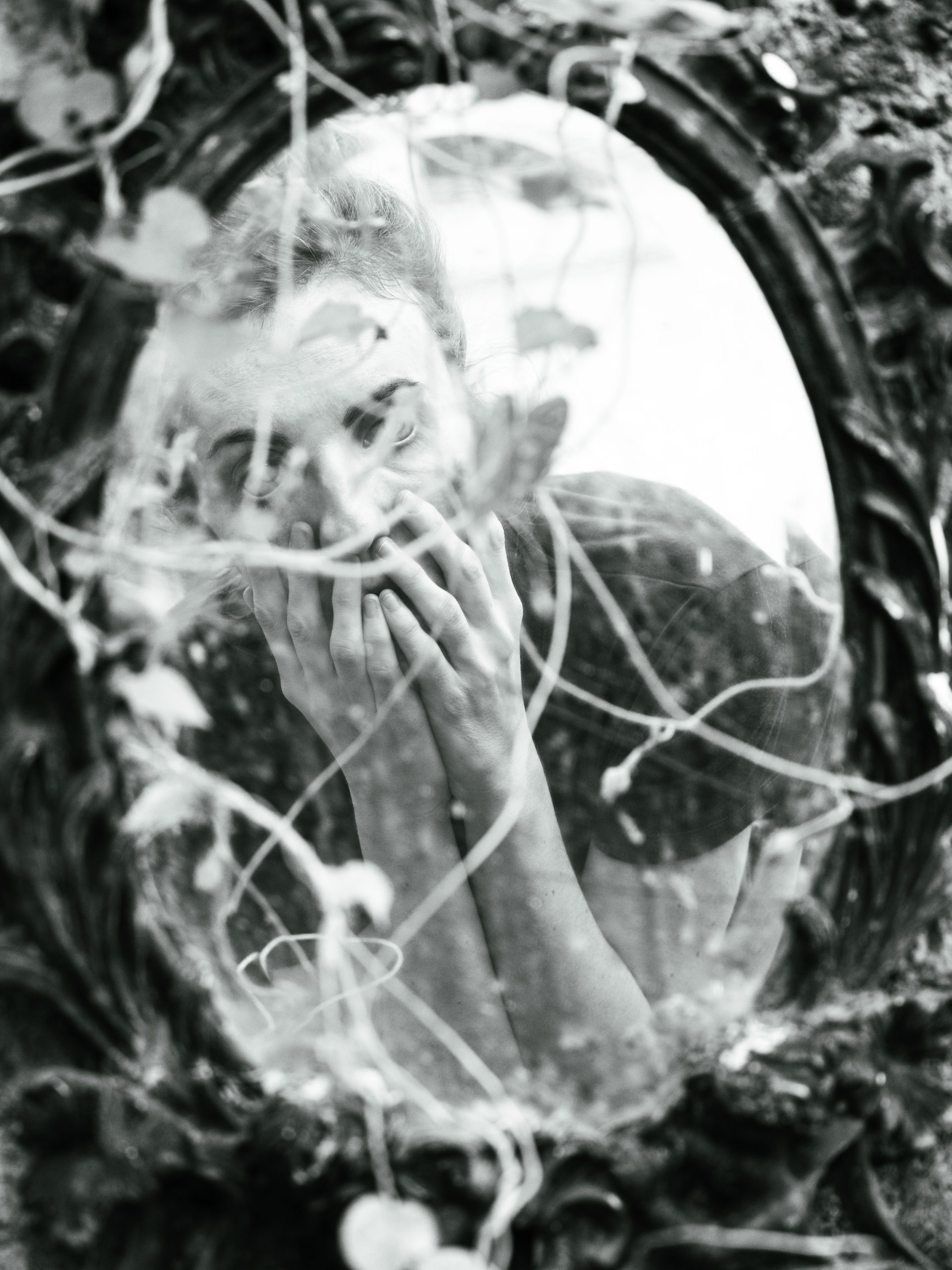 Artistic reflection of a woman in a vintage mirror surrounded by ivy. Reflet artistique d'une femme dans un miroir vintage entouré de lierre.