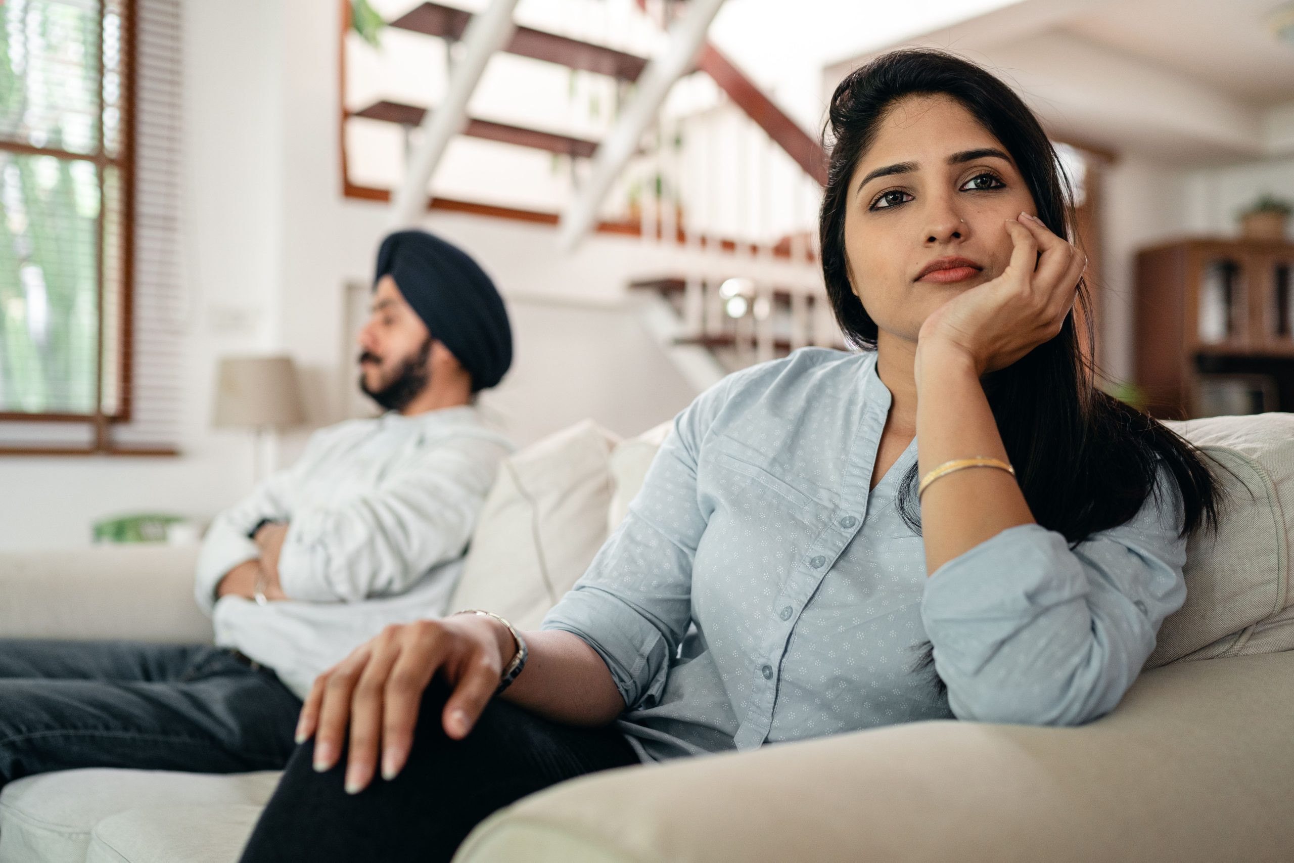 Young Indian couple sitting on different sides of couch and ignoring each other after arguing at home Jeune couple indien assis sur les différents côtés du canapé et s'ignorant l'un l'autre après une dispute à la maison