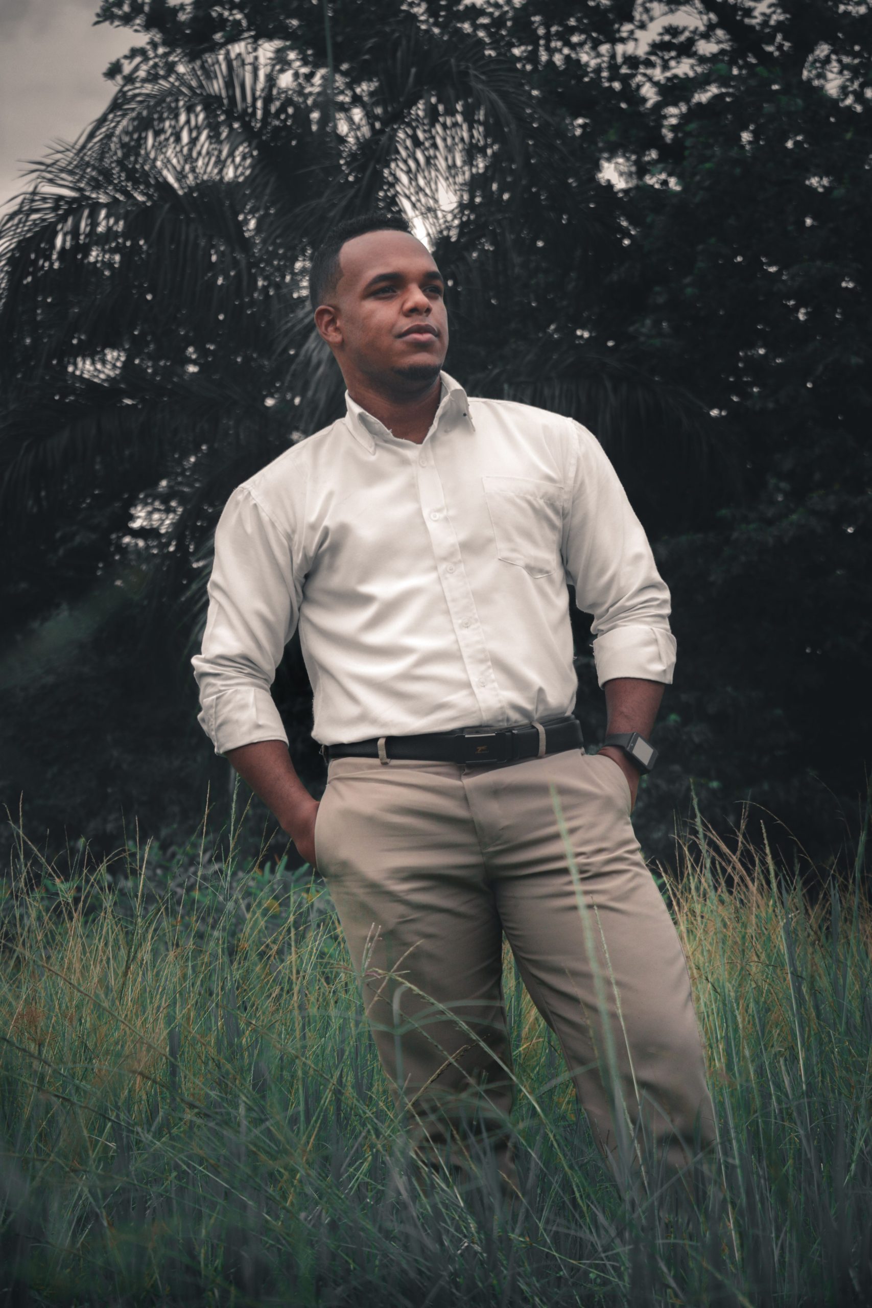 A stylish man in white shirt and khaki pants stands confidently in a field. Un homme élégant en chemise blanche et pantalon kaki se tient avec assurance dans un champ.