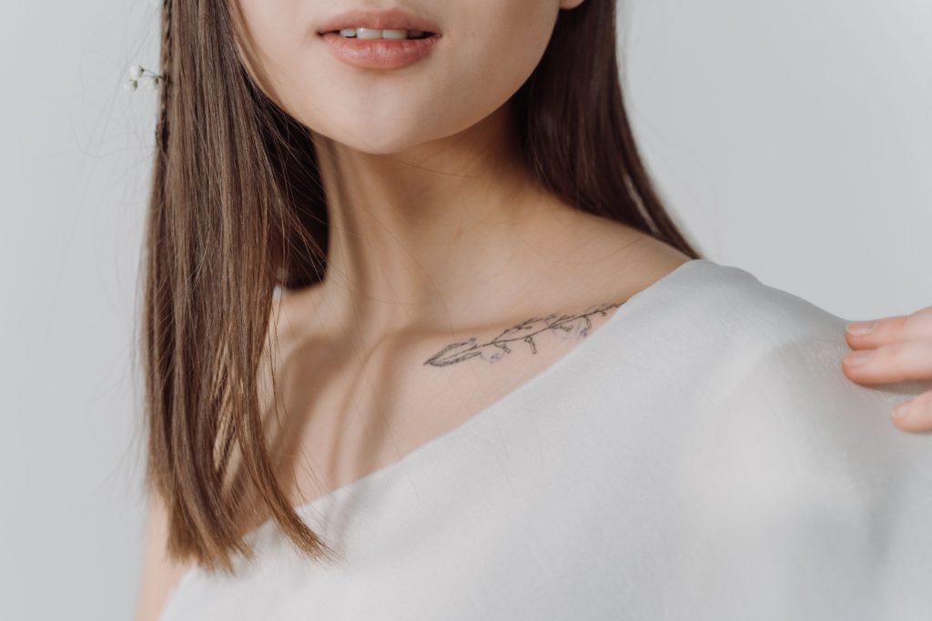 Gros plan élégant du tatouage de la clavicule d'une femme dans un haut blanc, mettant en évidence les détails subtils.