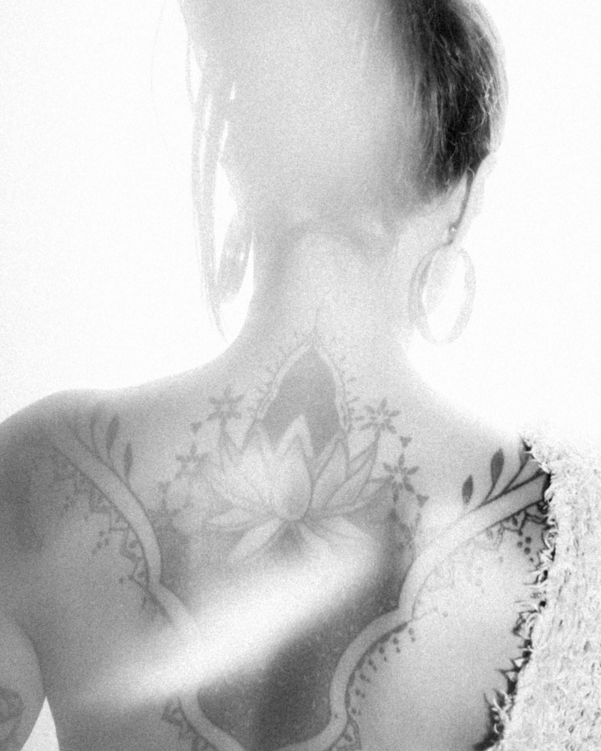 Black and white photograph showcasing a detailed tattoo on a woman's back under ethereal lighting. Photographie en noir et blanc mettant en avant un tatouage détaillé sur le dos d'une femme sous un éclairage éthéré.