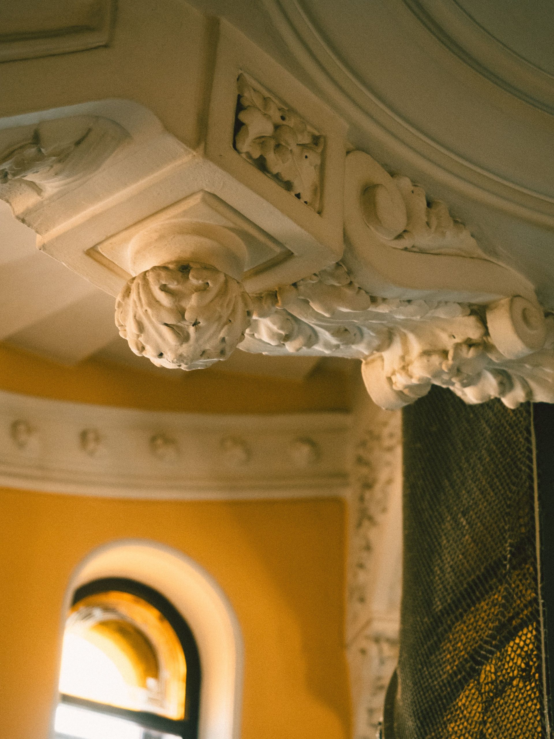 Detail of an ornate ceiling with intricate designs in warm lighting indoors. Détail d'un plafond orné avec des motifs complexes dans un éclairage chaleureux en intérieur.