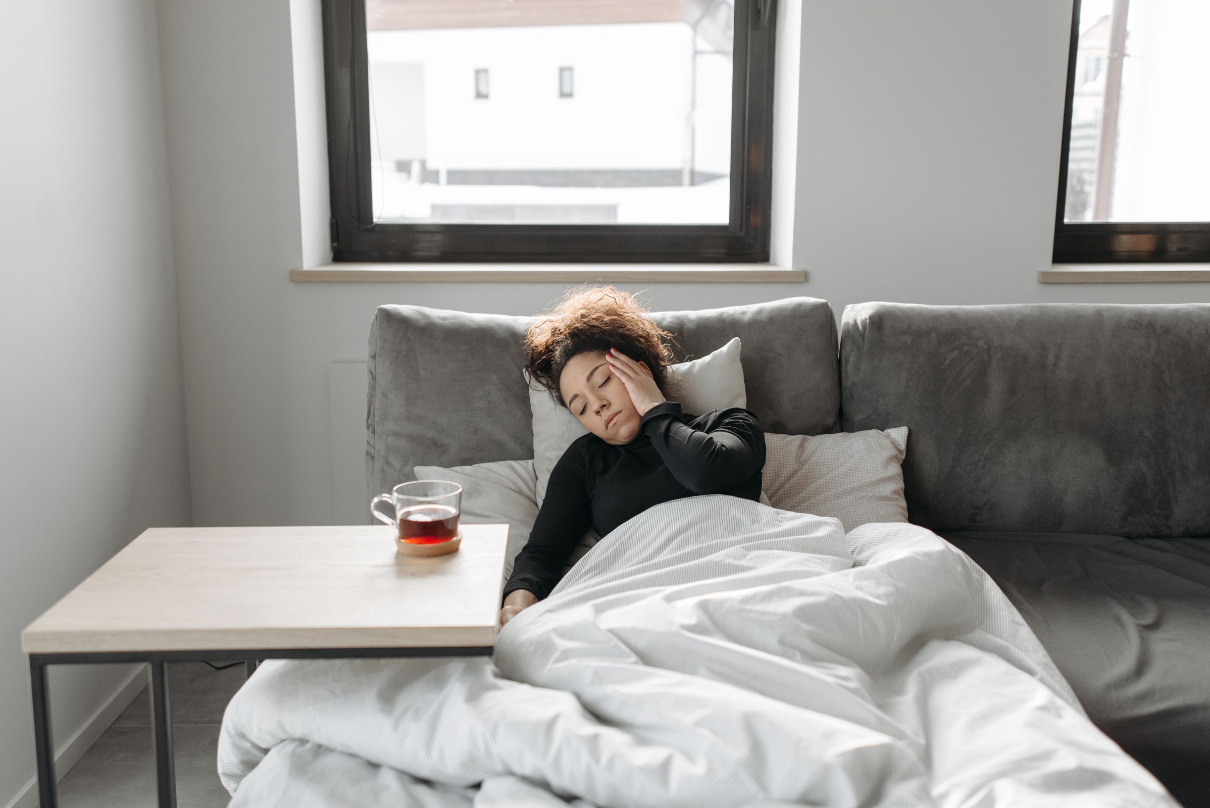 Femme reposant sur un canapé avec une tasse chaude, symptômes du Covid