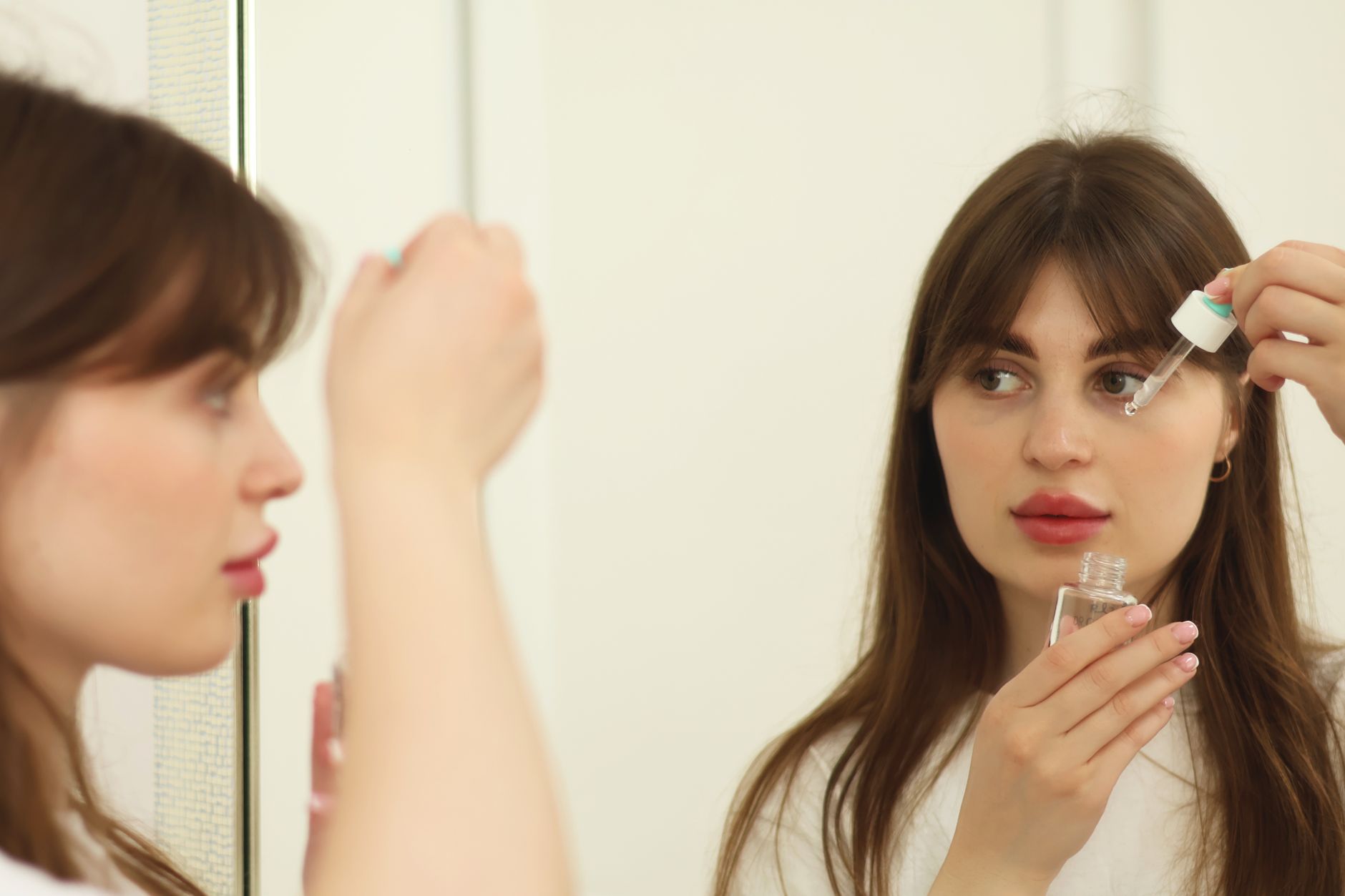 Femme applique un sérum visage devant un miroir